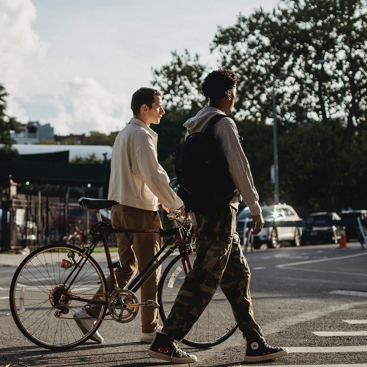 Two friends crossing the street - one on foot and one pushing a bicycle