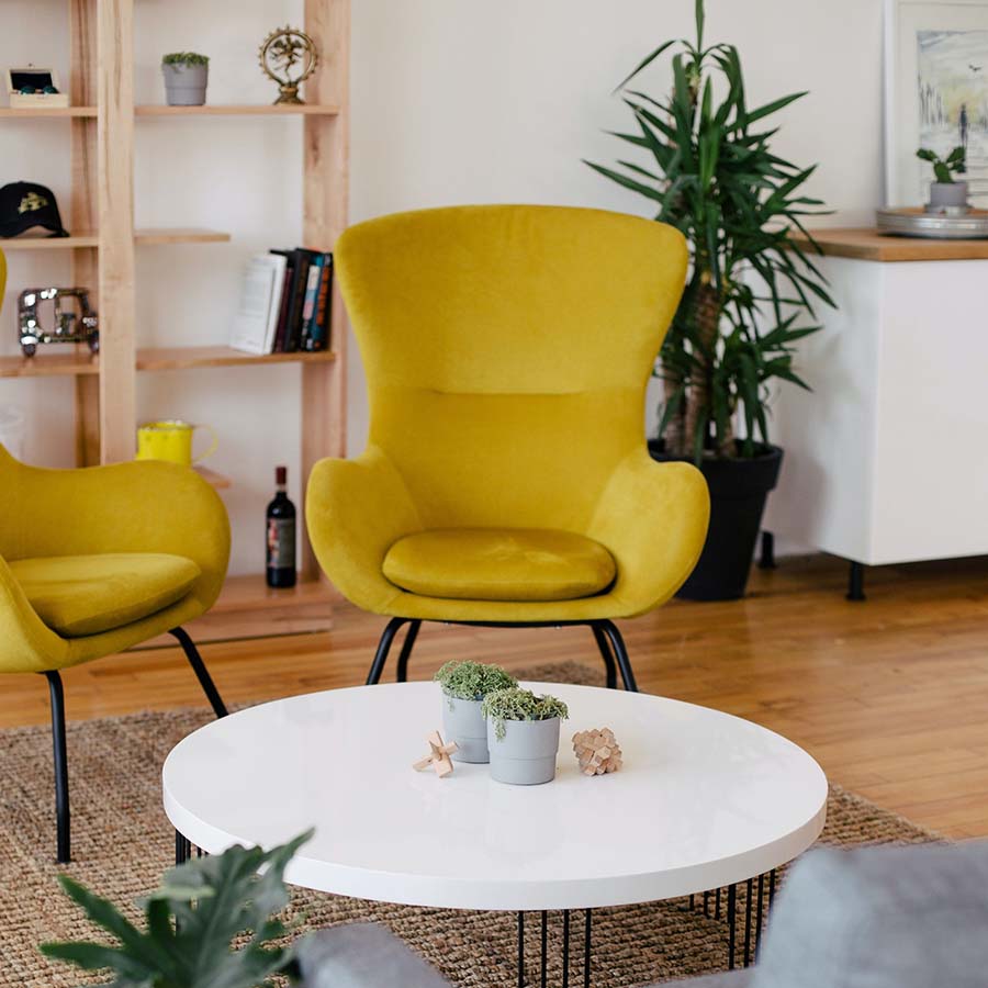 Living room with wood floor, round coffee table, modern leather lounge chairs, and tall potted plant.