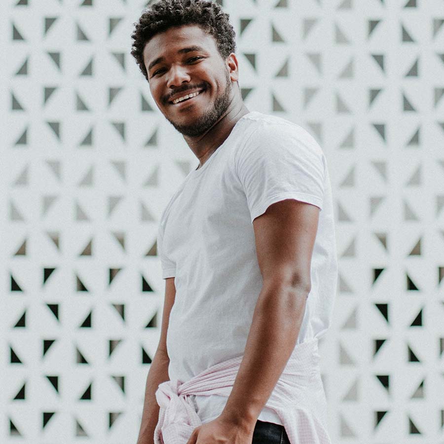 Smiling person with t-shirt standing in front of geometric wall.